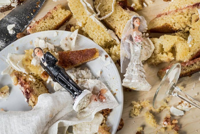 Wedding cake toppers laying atop a destroyed cake.