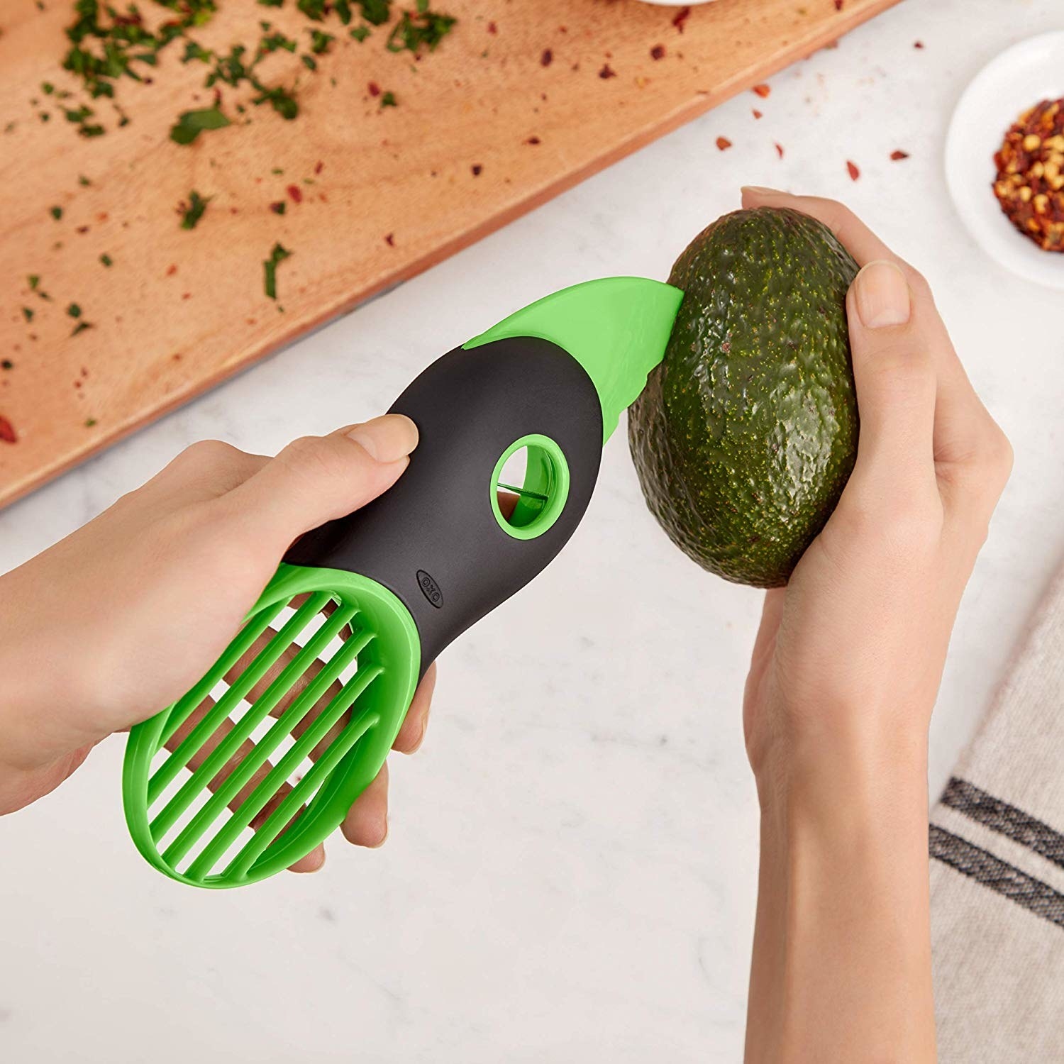 Hand using avocado tool to slice open avocado