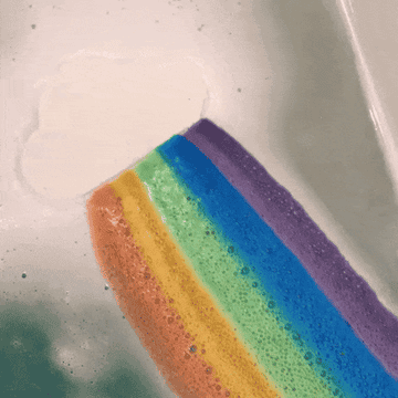 Bath bomb dissolving a rainbow into bath tub