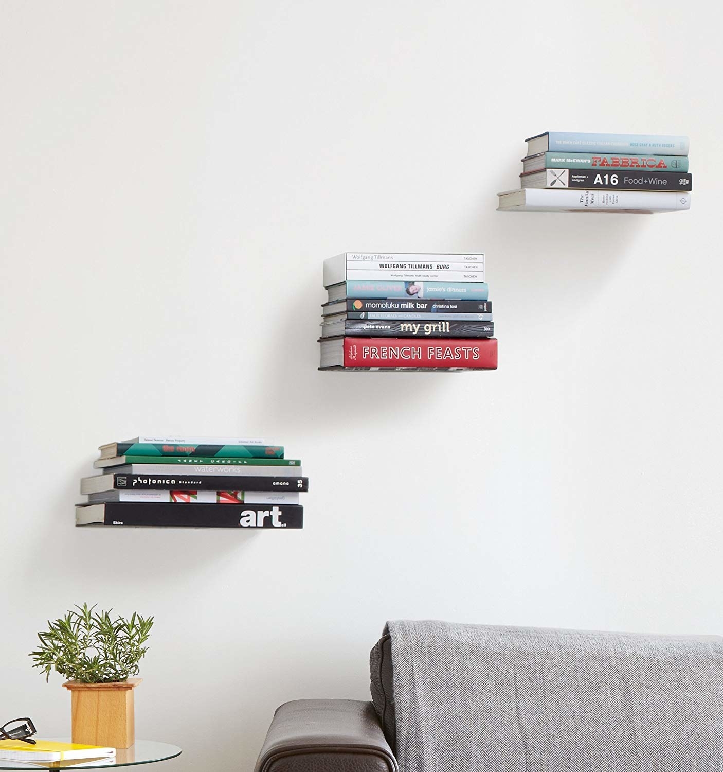 three stacks of books seeming to float on the wall above a couch
