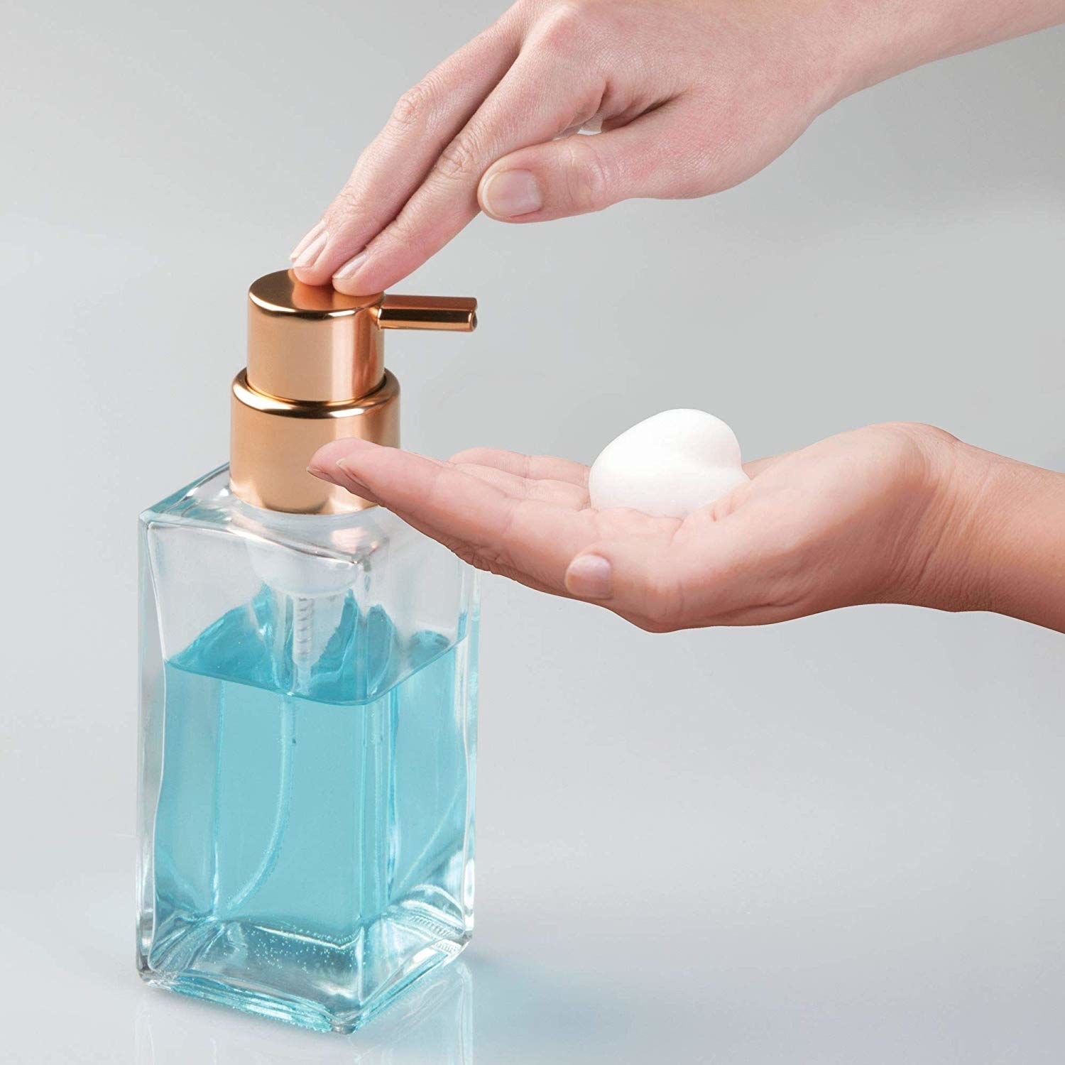 Model using the clear soap dispenser with light blue soap to dispense some foam onto their hand