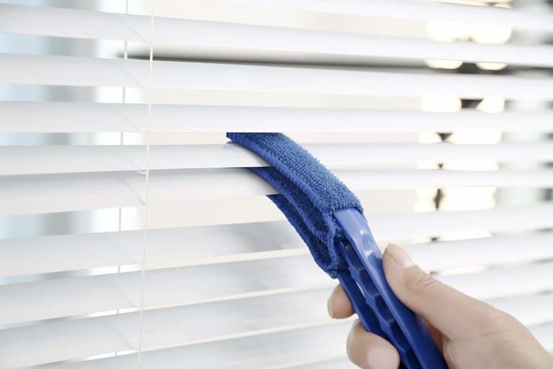 a hand using the blue duster to clean both edges of a blind