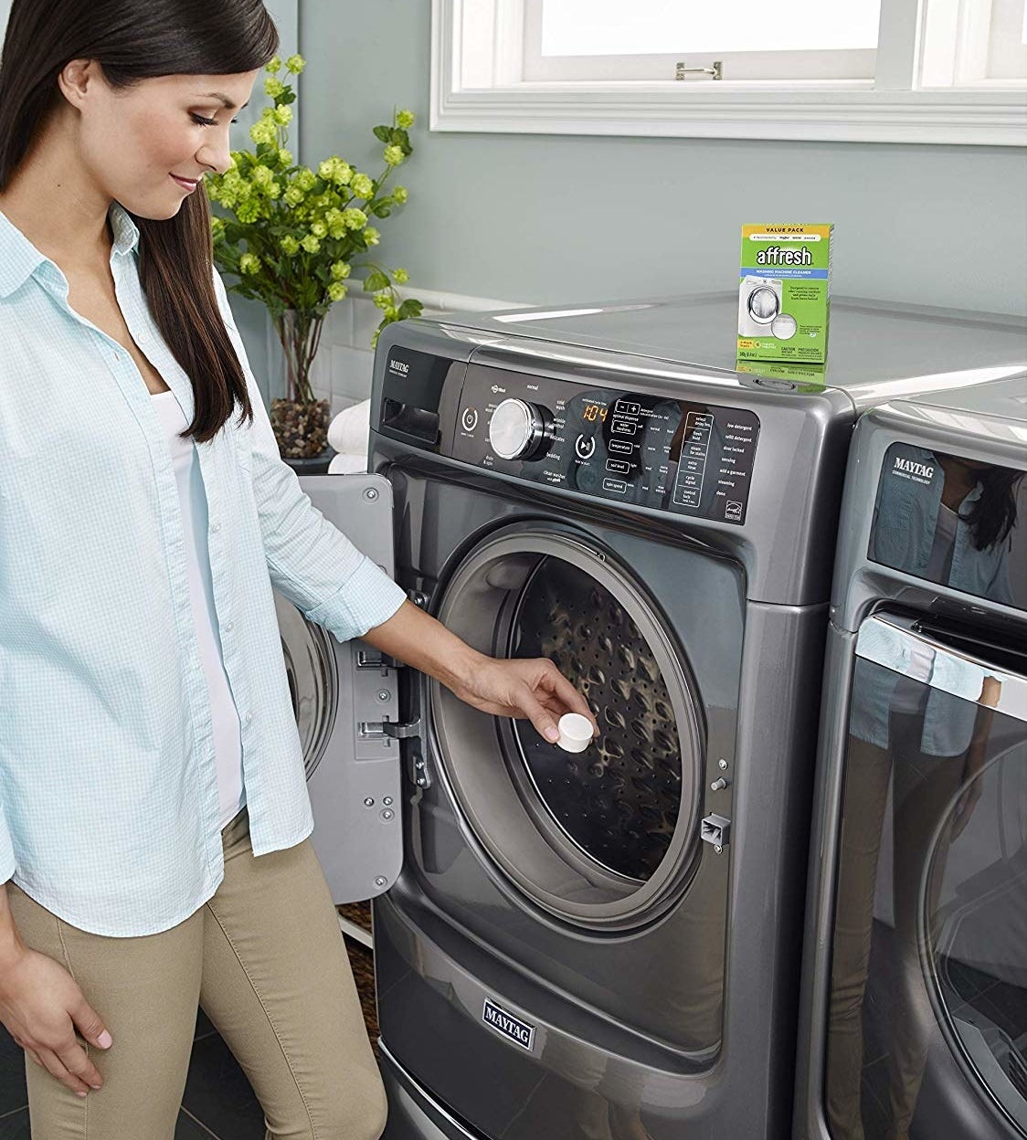 a hand holding a tablet above a washing machine