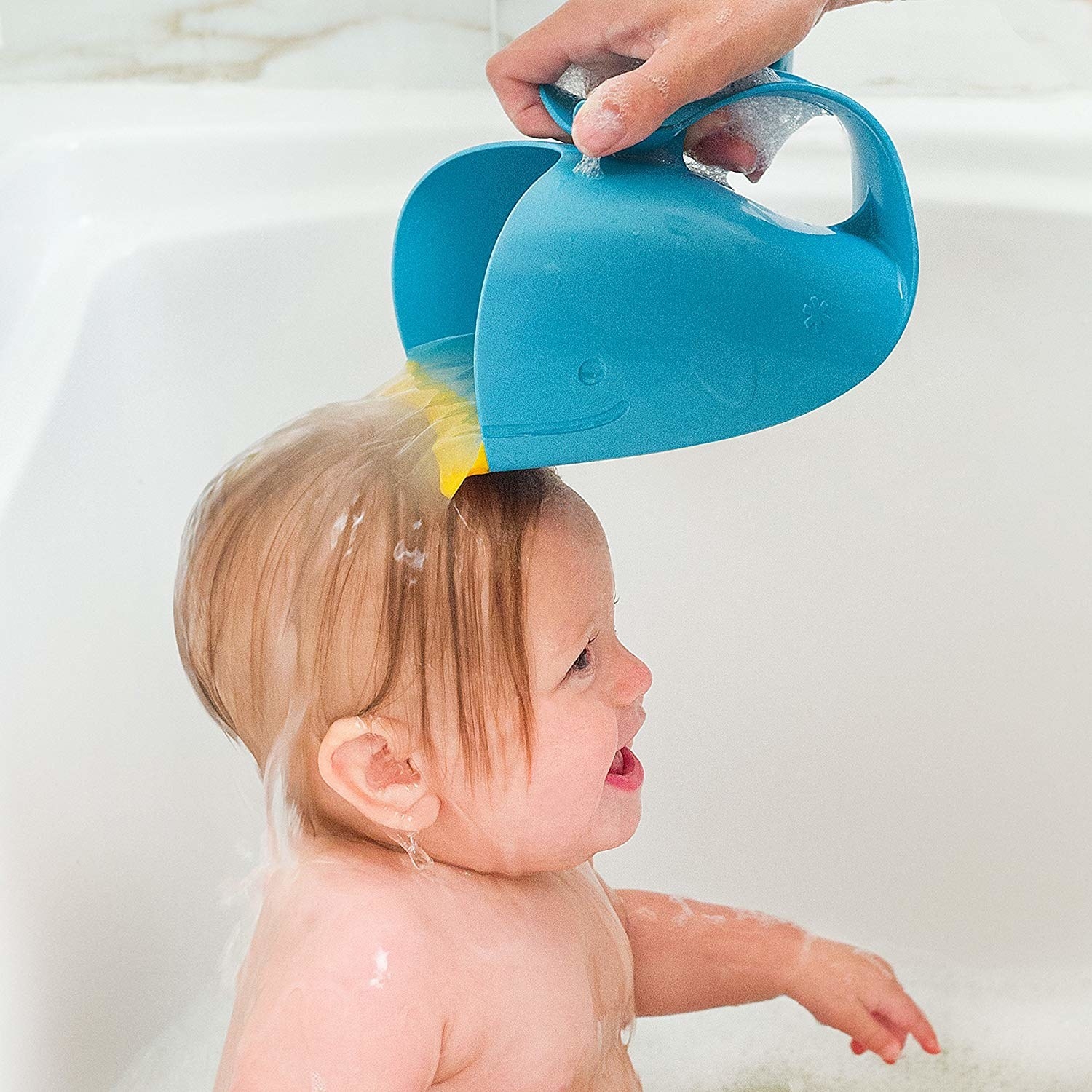 person pouring water on a baby's head using the whale-shaped rinser