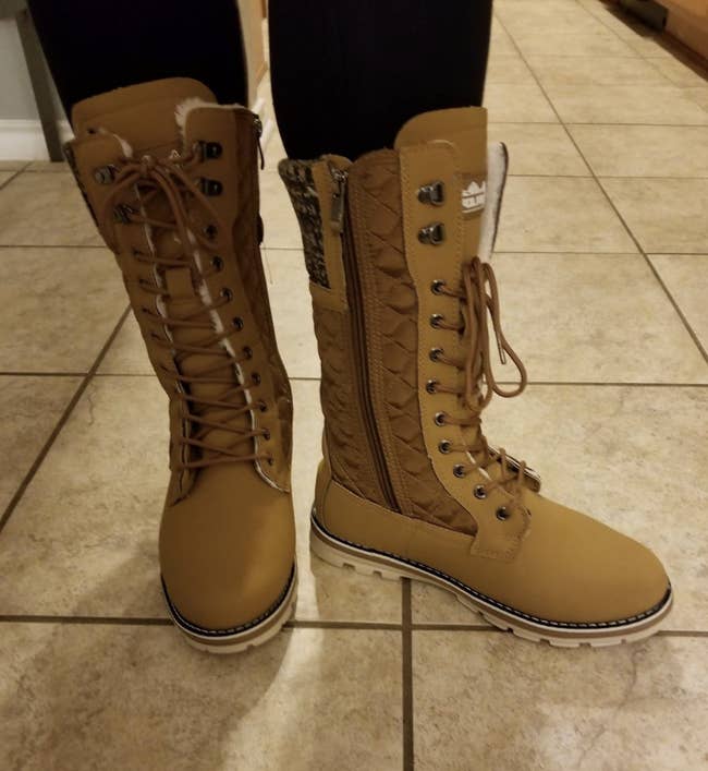 reviewer wearing the mid-thigh length lace-up boots in brown with a zipper along the inner side