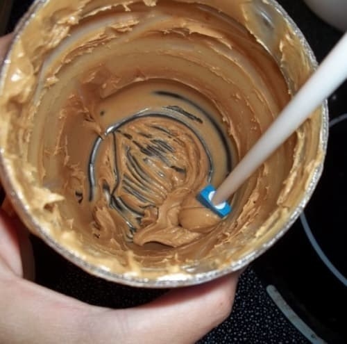 Person scraping out a large dollop of peanut butter from the bottom of nearly jar using the small, narrow, long-handled tool