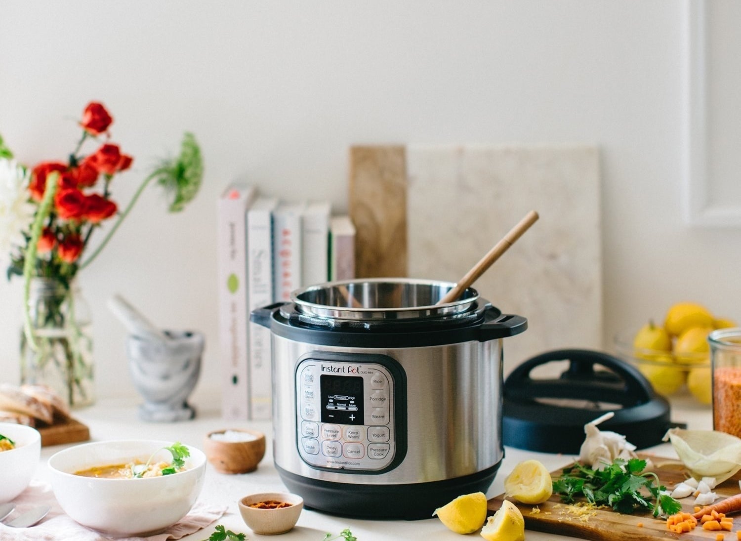 An instant pot on a counter with a wooden spoon and scattered ingredients