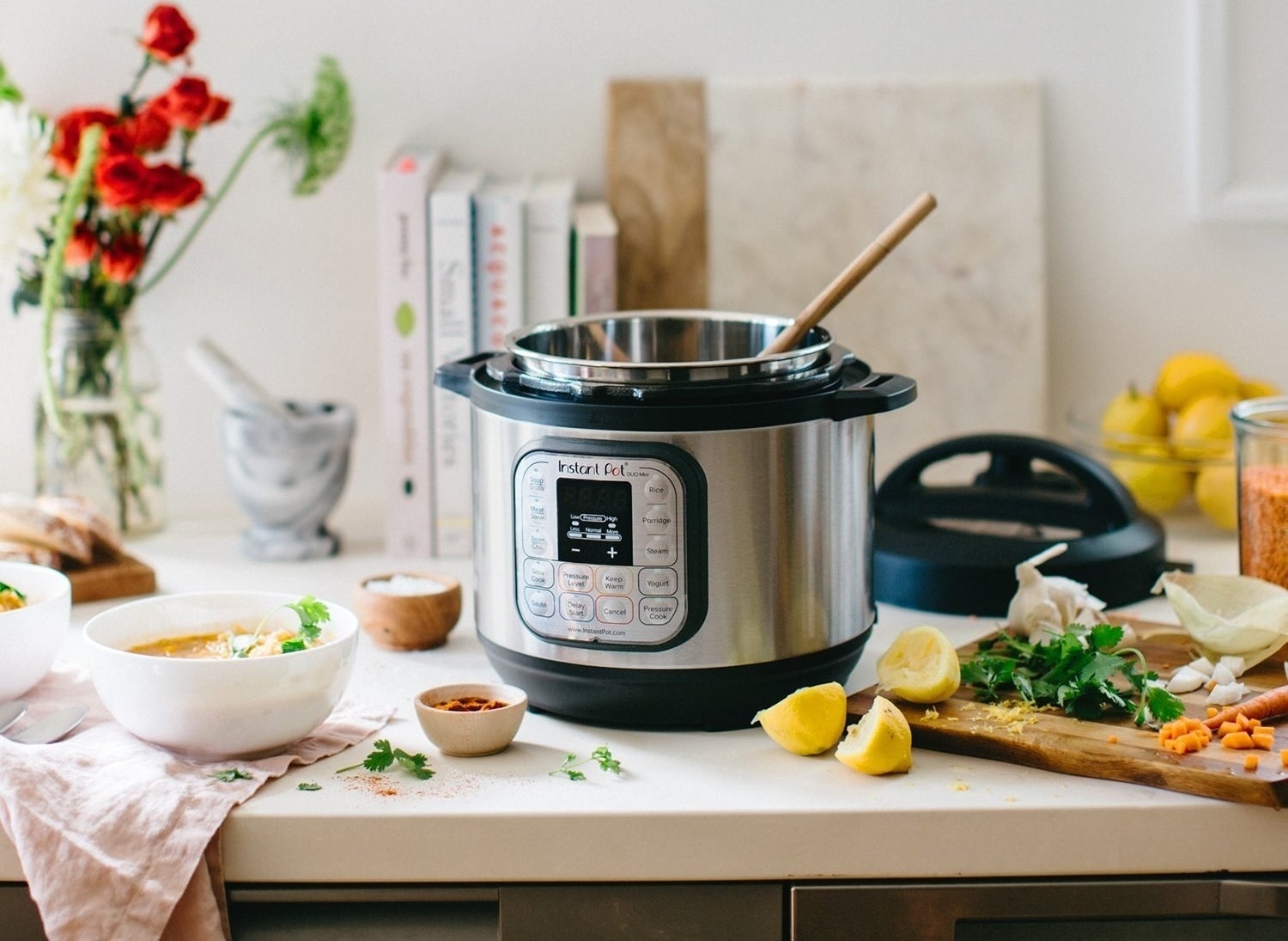 An instant pot on a counter with a wooden spoon and scattered ingredients