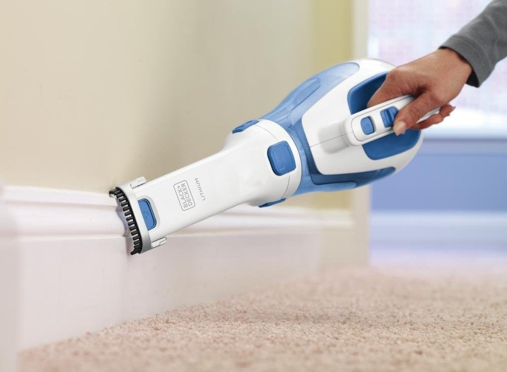 model cleaning a base board with a handheld vaccuum with a foot-long narrow attachment