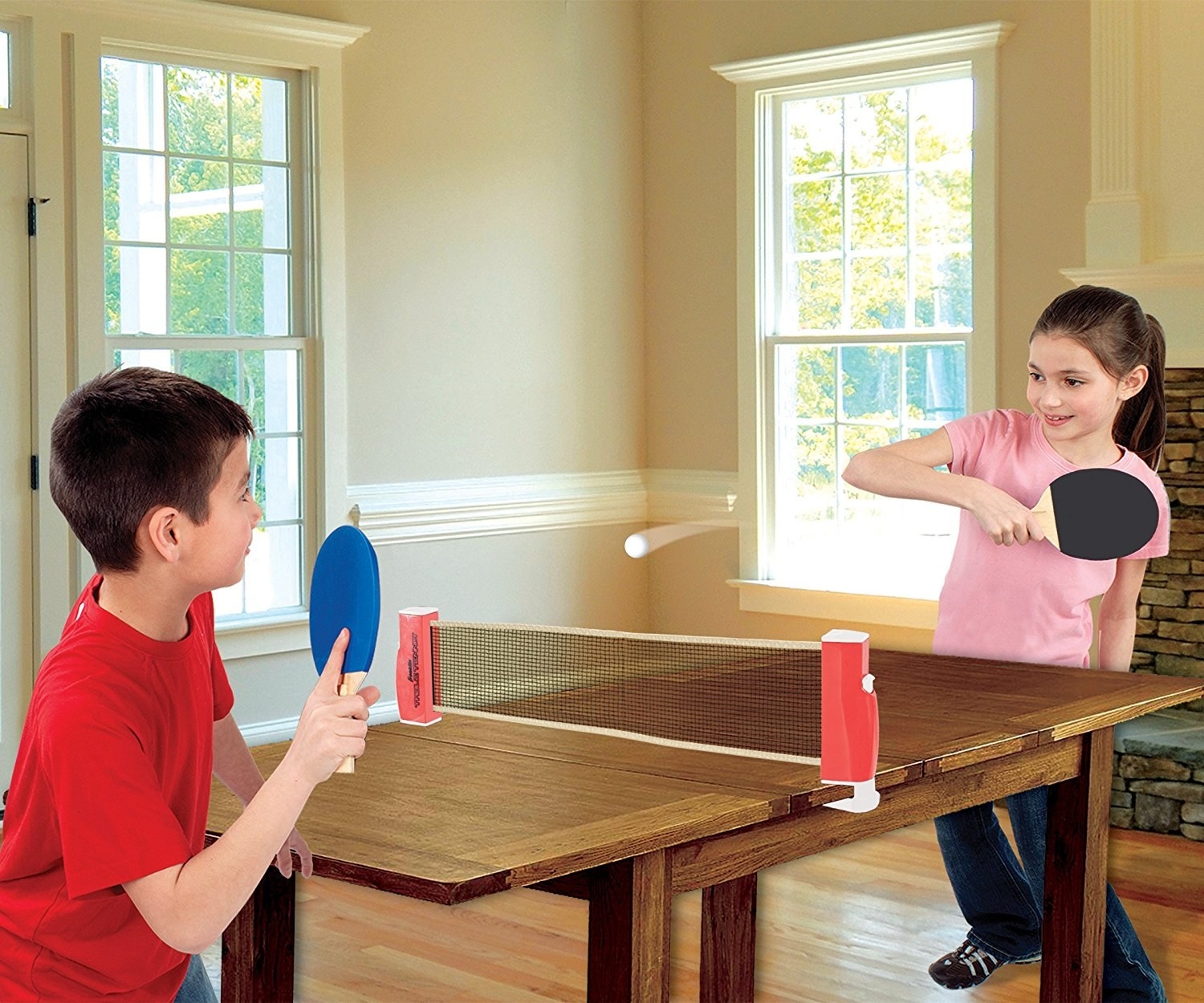 Two kids playing ping pong with a net over a wooden table