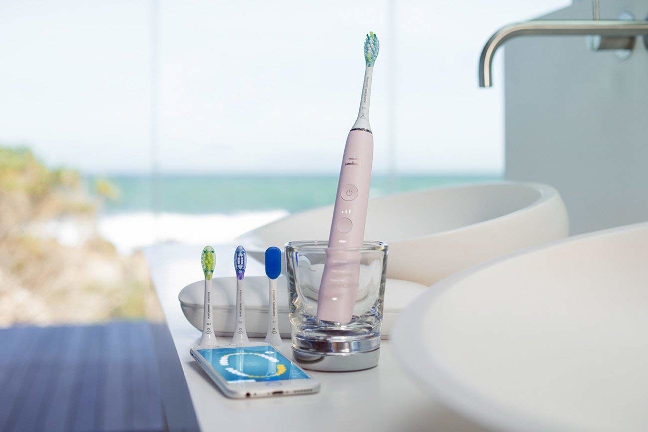 The pink toothbrush in a charging class with three extra brush heads and a phone showing the app