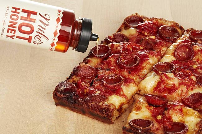 the bottle of the honey drizzling on a pepperoni pizza