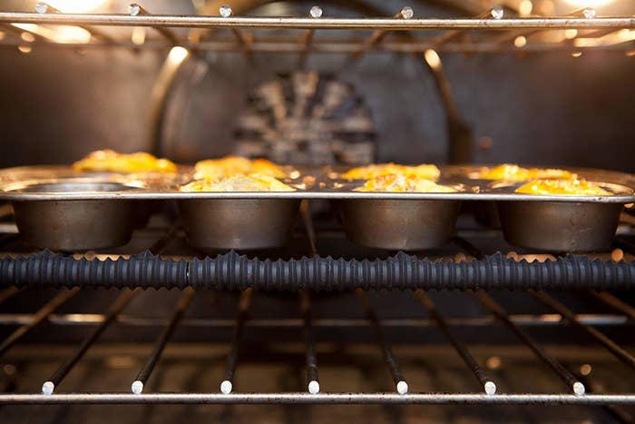 inside an oven with muffins baking and silicone guard on edge of oven rack
