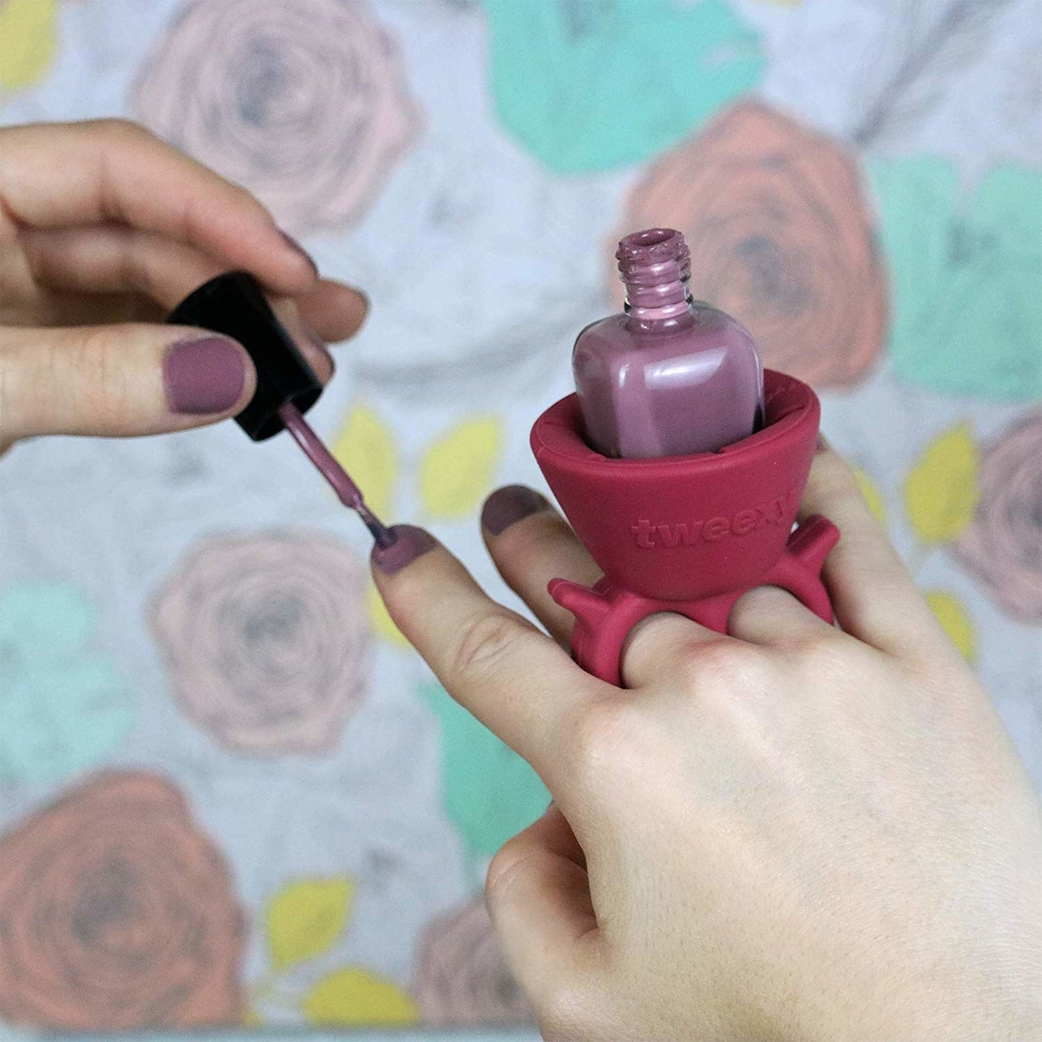 person&#x27;s hand with ring-like nail polish bottle holder on same hand that the person is painting their nails on 