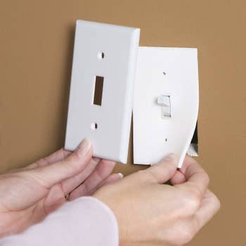 Hands installing the socket sealer beneath a light switch plate