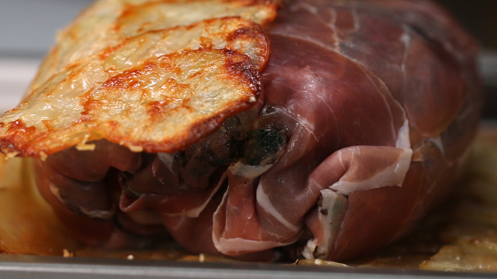 Ingredientsfor 6 servings1 medium white onion, finely diced¾ lb crimini mushroom, minced (340 g)4 cups fresh spinach, chopped (160 g)1 ½ tablespoons garlic, minced, dividedsalt, to tastepepper, to taste2 lb beef ribeye (910 g)3 tablespoons canola oil, divided½ lb prosciutto, sliced (225 g)¼ cup mayonnaise (55 g)½ teaspoon dried thyme1 tablespoon lemon juice2 large russet potatoes, washed and peeled2 cups grated parmesan cheese, divided, plus more for sprinkling (230 g)PreparationPreheat the oven to 350˚F (180˚C).Pour 1 tablespoon of oil into a medium skillet over medium heat and sauté the onion, mushrooms, and spinach for about 5-7 minutes, or until the onions begin to turn translucent. Add 1 tablespoon of garlic, salt, and pepper and cook, stirring occasionally, until all the liquid evaporates and the mixture becomes a thick paste. Remove from the pan and let cool completely.Generously season the rib eye all over with salt and pepper. Heat the oil in a medium skillet over medium-high heat. Sear the meat for 3-5 minutes on all sides, until a crust has formed all over. Let rest on a wire rack for 10 minutes.Arrange overlapping sheets of plastic wrap until you have a surface twice the length and width of the rib eye. Lay overlapping strips of prosciutto on the plastic in an even layer, making sure the prosciutto sheet is large enough to cover the rib eye. Spread the cooled mushroom mixture evenly over the prosciutto.In a small bowl, stir together the mayonnaise, remaining ½ tablespoon minced garlic, ½ teaspoon salt, the thyme, and lemon juice. Generously brush the rib eye with the garlic mayo, then place the rib eye in the center of the prosciutto-mushroom sheet.Keeping everything even and tight, wrap the rib eye with the prosciutto, using the plastic wrap to help wrap it tightly and to seal the ends. Tuck the ends of the plastic wrap underneath the wrapped rib eye to keep its shape and chill in the refrigerator for 30 minutes.Using a knife or mandoline, carefully cut the potatoes into slices ⅛-inch (3 mm) thick and lay on paper towels. Sprinkle the potato slices with salt and let sit for 10 minutes to draw out any excess moisture. Pat the potatoes dry.Evenly sprinkle 1 cup (115 g) of Parmesan cheese over a parchment-lined baking sheet.Arrange the potato slices in overlapping rows over the Parmesan until the pan is covered. Sprinkle the remaining cup of Parmesan evenly over the potatoes.Bake for 30 minutes, until slightly golden and the potatoes are still flexible. Remove the potatoes from the oven and increase the heat to 400˚F (200˚C).Place the chilled, prosciutto-wrapped rib eye in the center of the potato sheet. Fold the potatoes over the rib eye and peel back the parchment. Sprinkle Parmesan under the seam (it will help seal the potato layer) and all over the top.Loosely cover the pan with foil and bake for 30 minutes. Remove the foil and bake for 20 minutes more, or until the potatoes are golden brown and the internal temperature of the beef is at least 135°F (57°C) for medium-rare. Rest for 10 minutes before slicing.Enjoy!