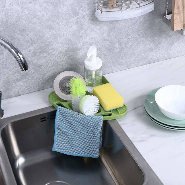 kitchen sink with a corner caddy with a dishcloth hanging from it and dish brushes, a sponge, and hand soap contained on it