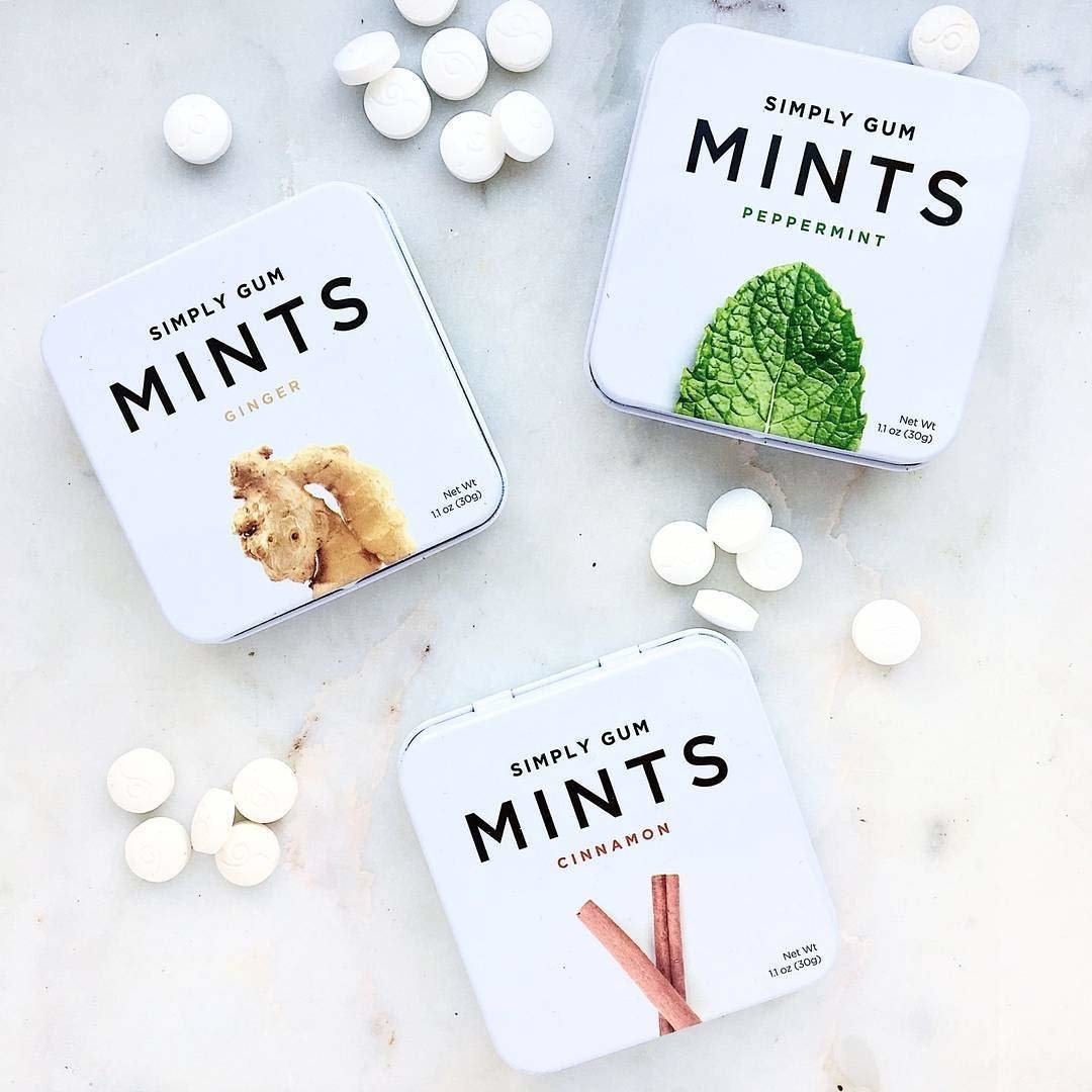 Three square mint tins with small pill-sized mints on table around them 