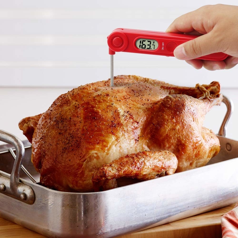 The red thermometer with its stainless steel reading needle inserted into a roasted turkey