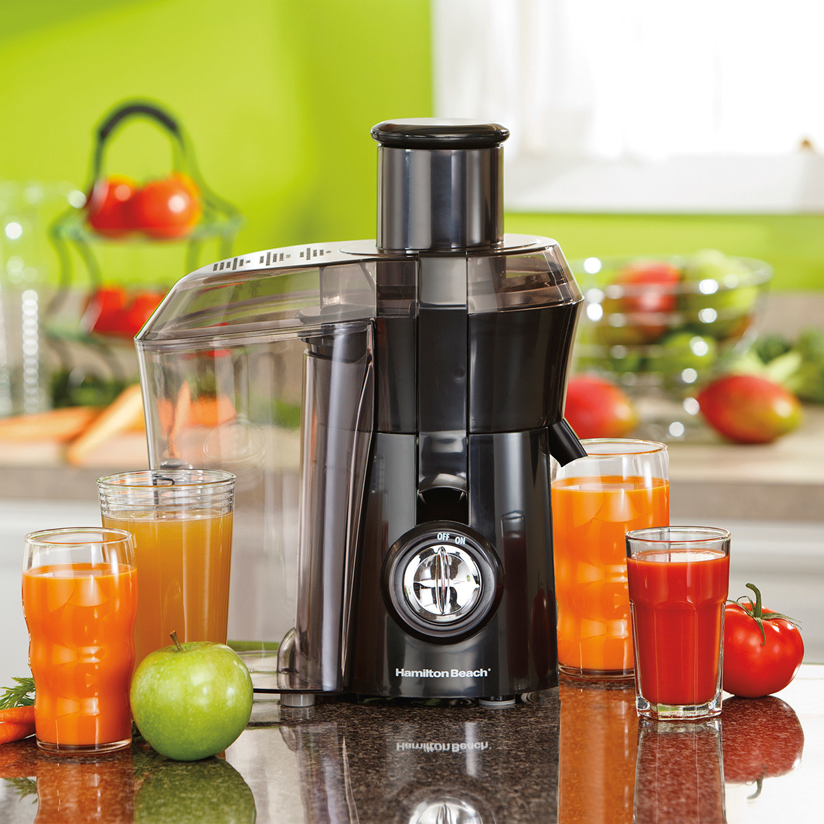 The juice extractor on a counter surrounded by cups of different juice as well as apples and tomatoes