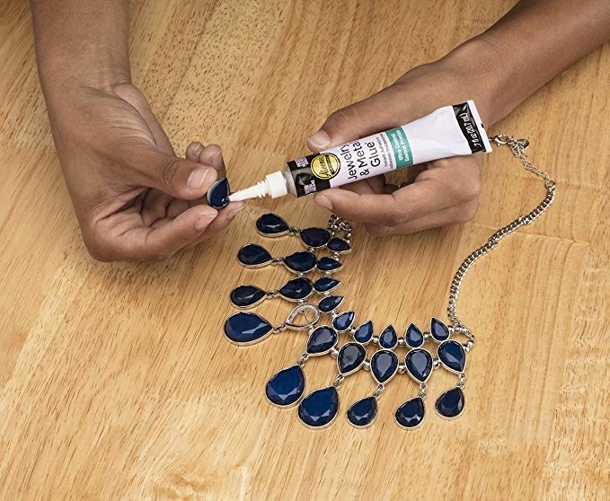 hands gluing a loose gem back into a statement necklace