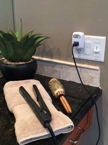 a hair straightener resting on a towel on a bathroom counter plugged up to the timer 