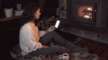 a model reading the Kindle by a fireplace