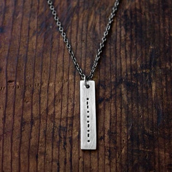 Metal plate necklace on chain in long rectangle with morse code dots and lines pressed into the plate 