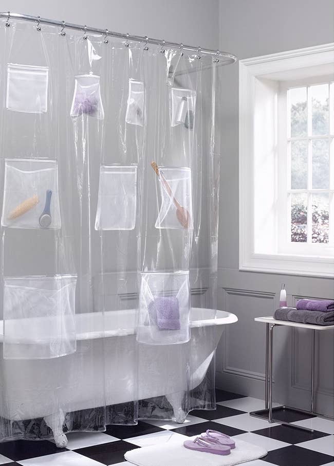 A clear shower curtain around a clawfoot bathtub with pockets holding shampoo bottles, washcloths, and other bathtime accessories