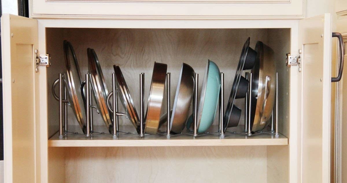 An open cabinet with pots, lids, and baking sheets neatly nested in a steel rack