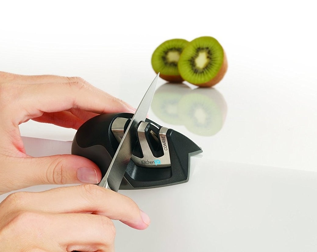 a pair of hands using the knife sharpener next to a sliced kiwi