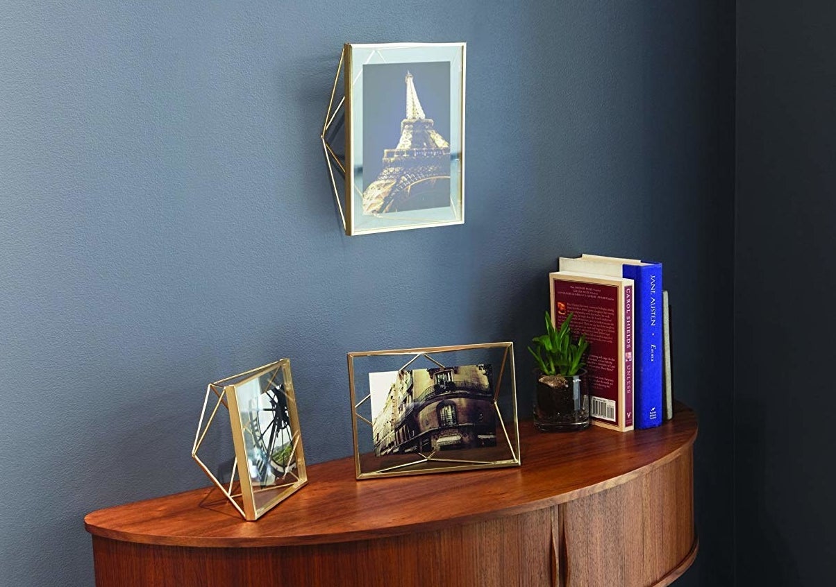 a brass photo frame hanging above a console table with two other brass frames on top of the table