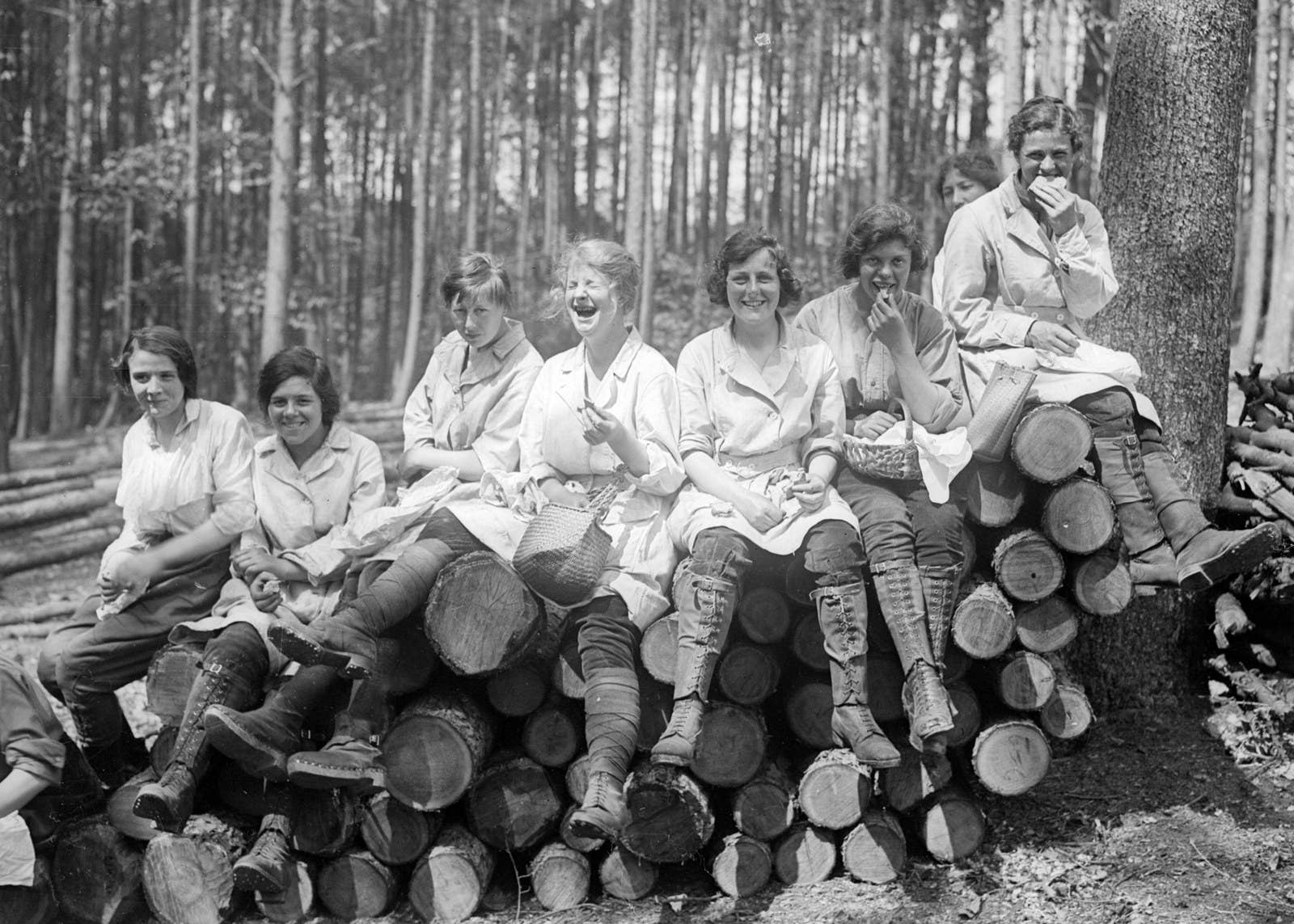 Women forestry workers sit on a pile of logs enjoying their lunches, 1918.