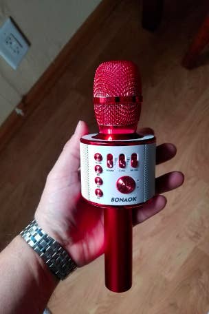 A reviewer's hand holding the red mic with buttons around the center