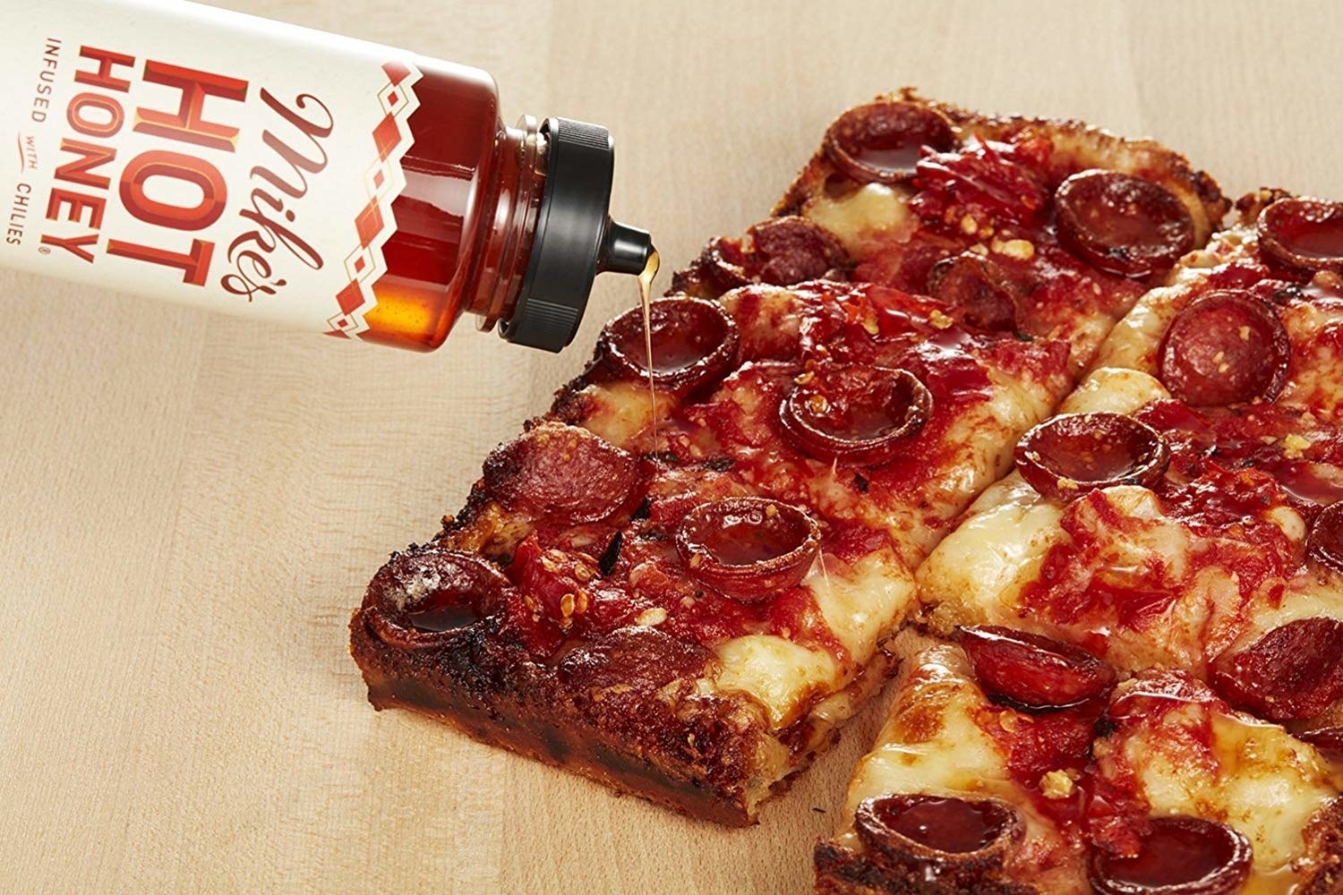 The bottle of honey honey pouring onto a pepperoni pizza