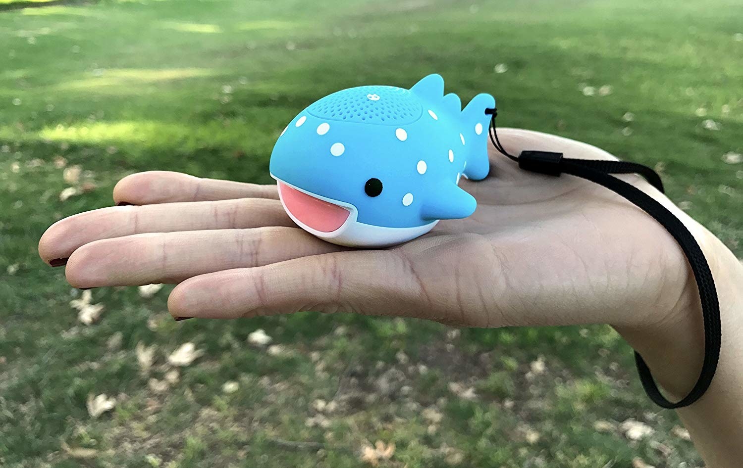 A hand holding the small whale-shaped speaker with a wrist loop