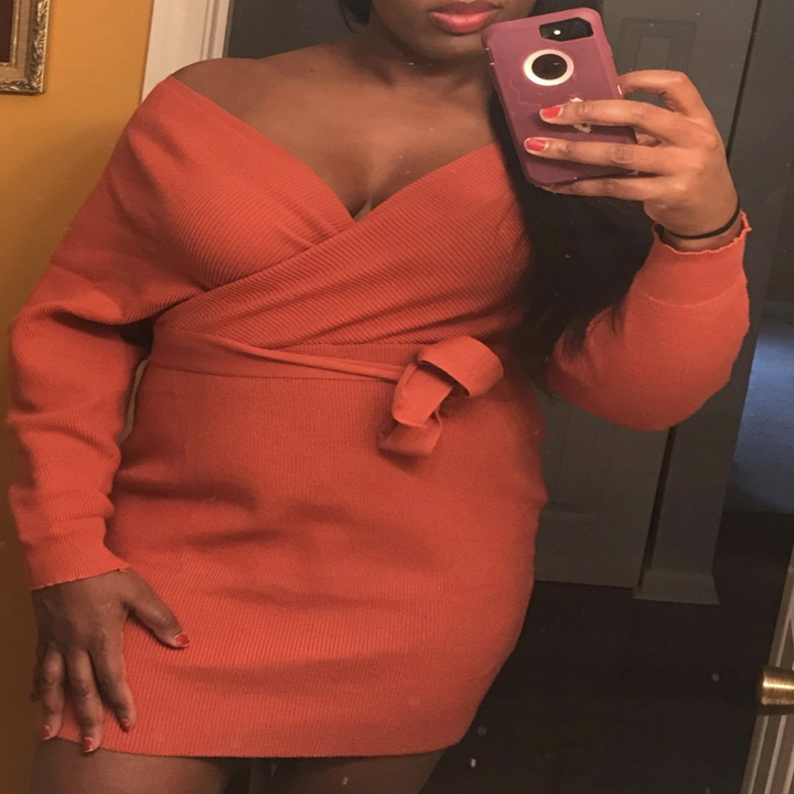 Closeup of a reviewer wearing the sweater dress off the shoulder with a deep v-neck and tie around the waist in orange