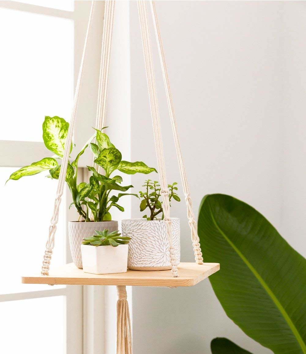 The wooden shelf hanging from white macrame and a tassel underneath
