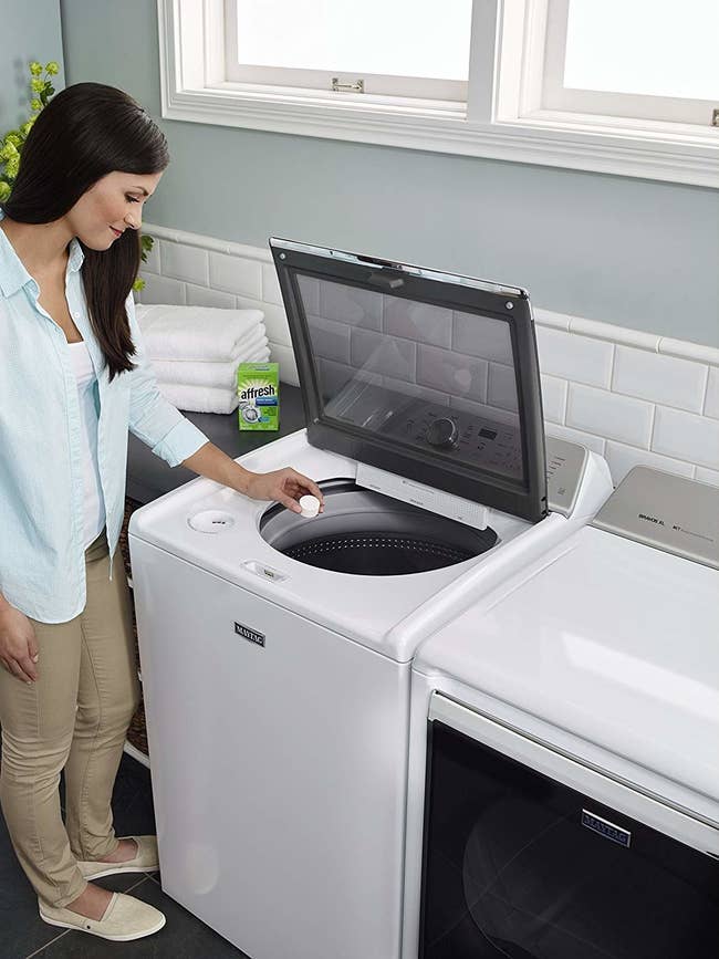 model putting a cleaning tablet into a top-load washing machine