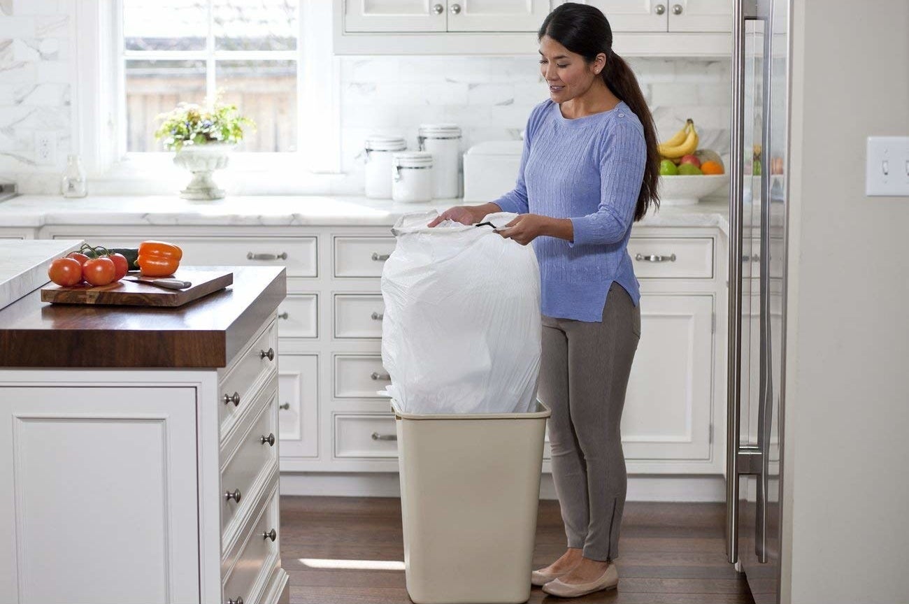 model taking bulky bag out of a trash can in a kitchen