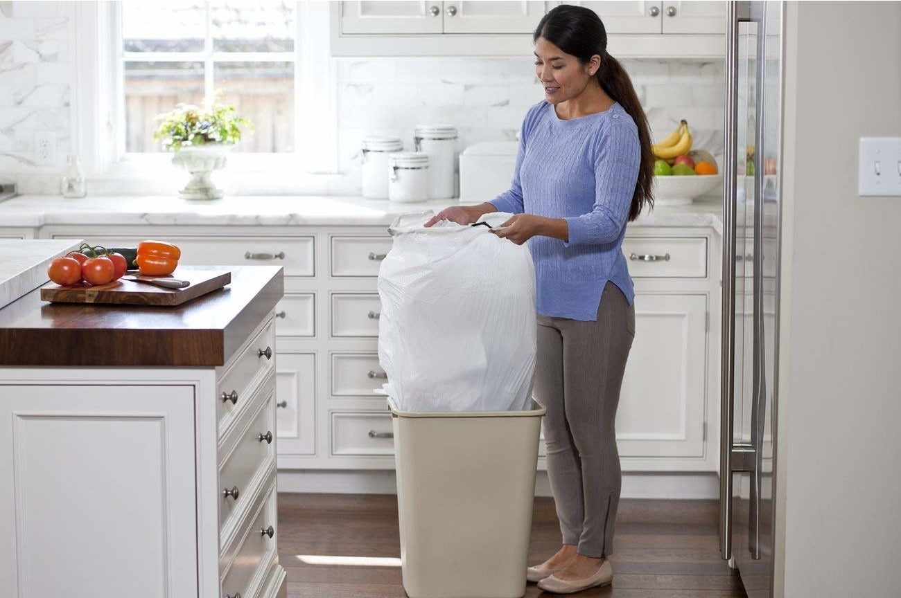 model taking bulky bag out of a trash can in a kitchen