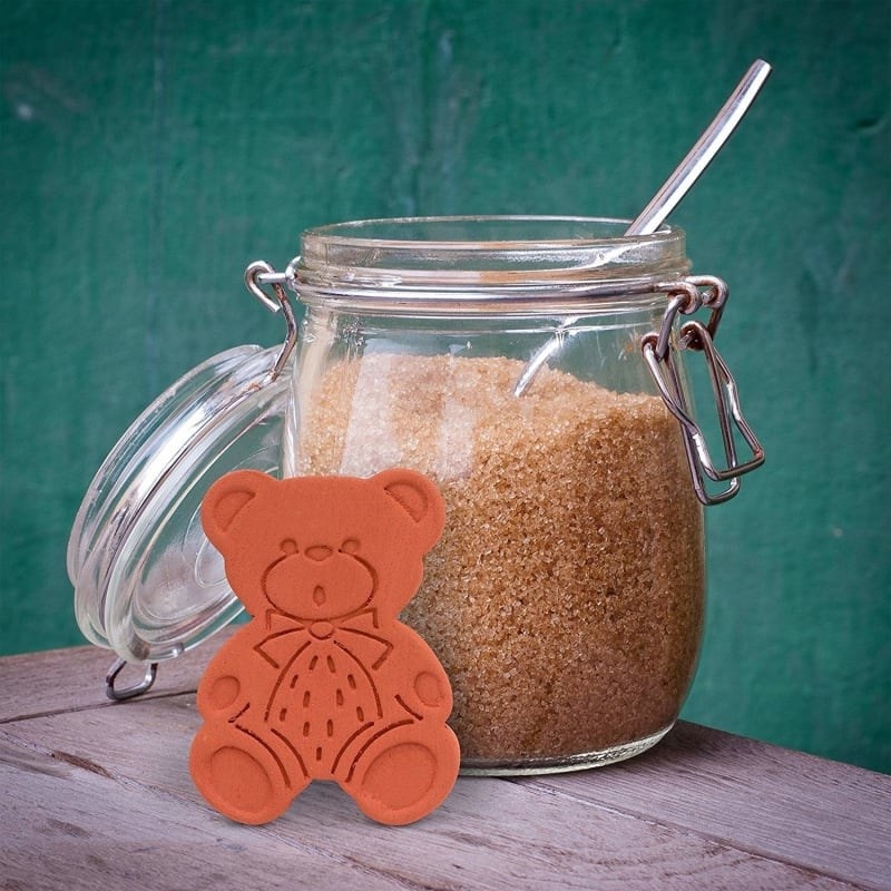 product shot of terracotta bear leaned up against an open glass canister of brown sugar