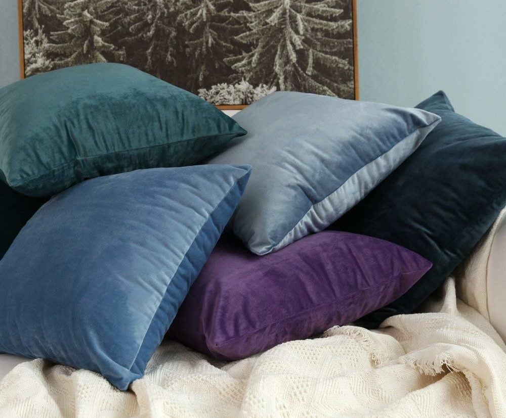 a teal, blue, light blue, purple, and navy blue velvet pillowcases on a bed