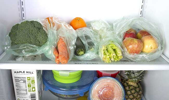 A fridge shelf with produce in the green-tinted bags