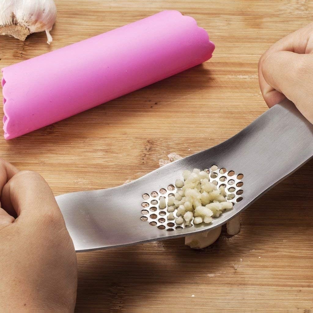 The pink silicone tube and hands using the metal press to mince garlic
