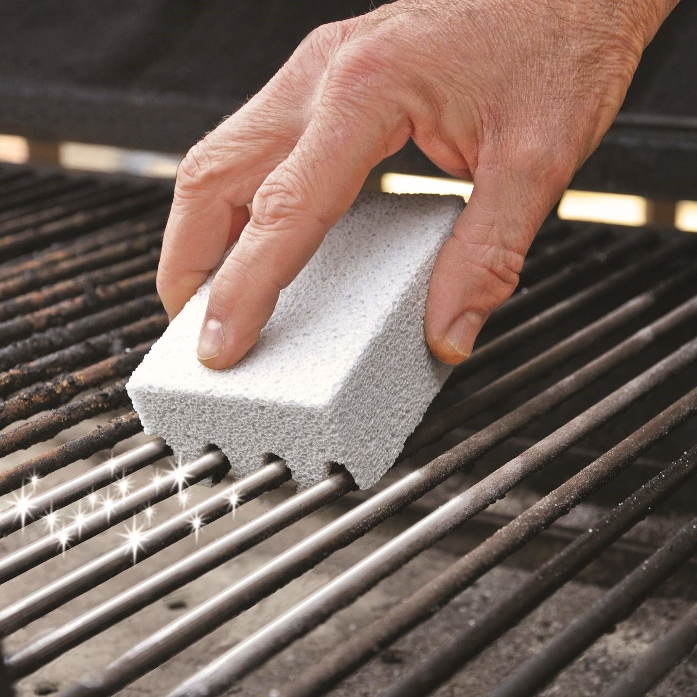 A person using the grill scrubber to clean a grill