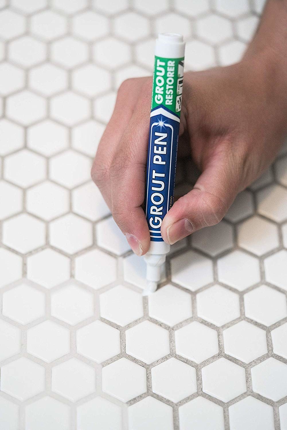 Grout pen in hand filling in dark tiles with white, matching cover