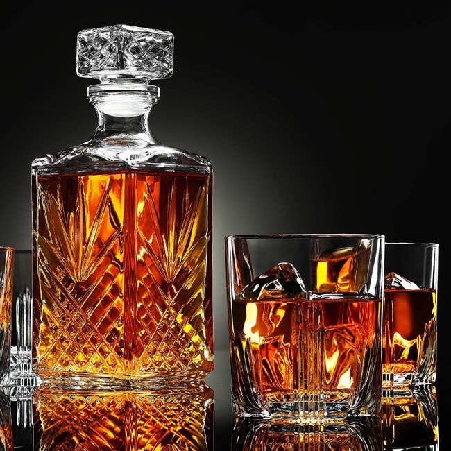 crystal cut decanter and two matching drinking glasses filled with brown liquor