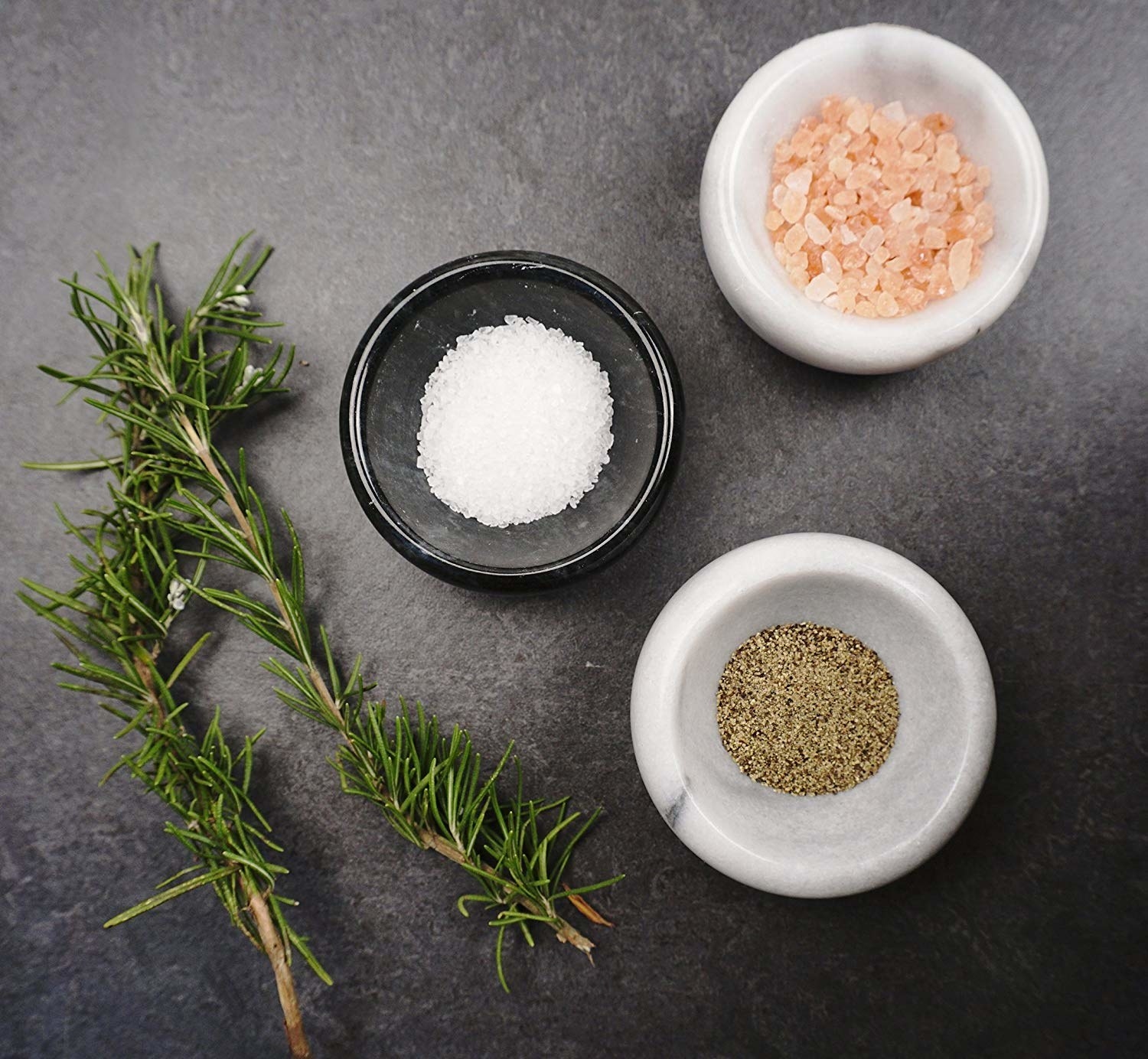 Top shot image of a sprig of thyme and marble bowls with different seasonings inside each 