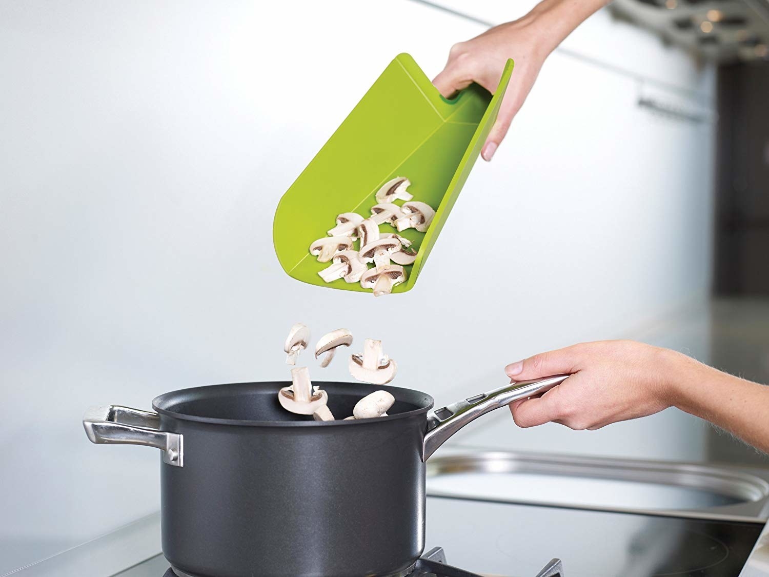 Tri-folded cutting board spilling mushrooms into pot on stovetop